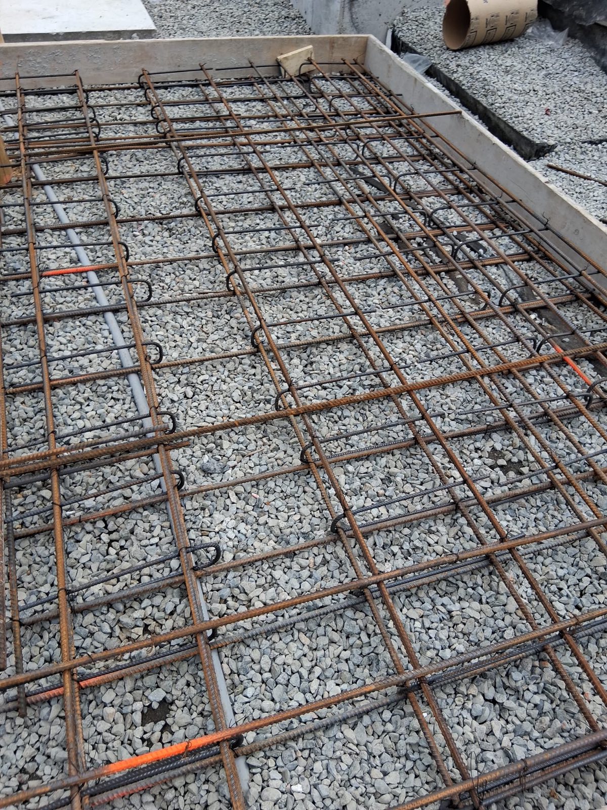 Reinforced concrete slab with tied rebar mat and conduit over compacted gravel